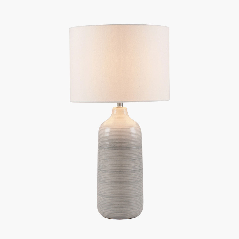 The Venus Blue and Grey Ombre Ceramic Table Lamp shown here with its bulb illuminated