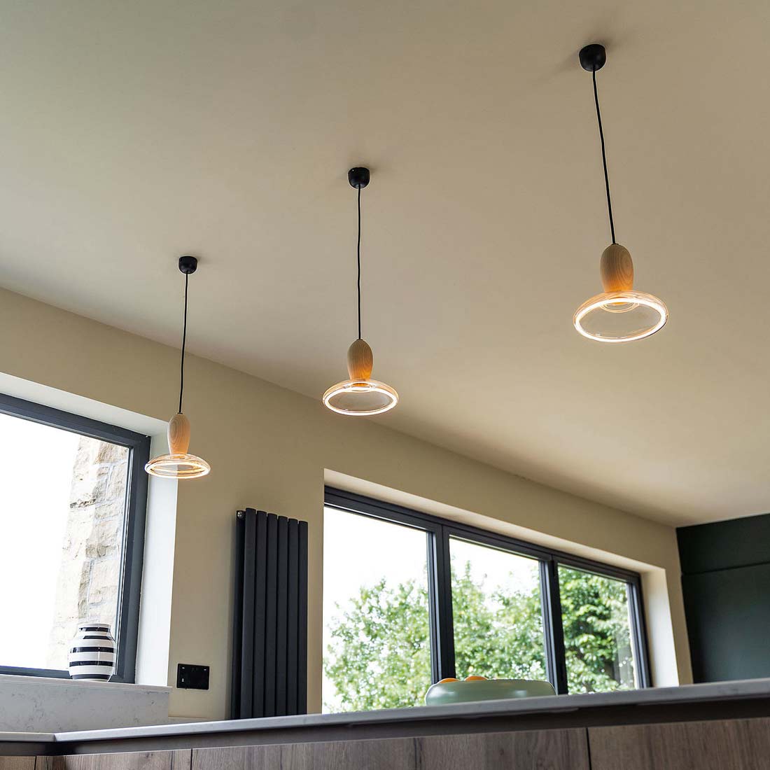 Three Well Lit Ash Wood Pendant Lights supplied by South Charlotte Fine Lighting are pictured lighting a breakfast bar